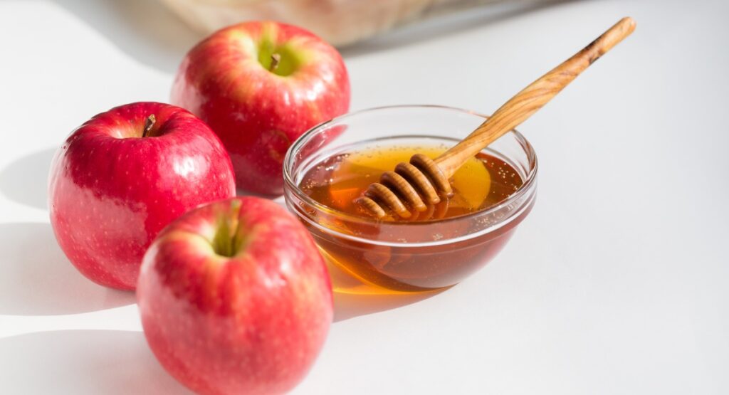 3 red apples around a small bowl of honey 